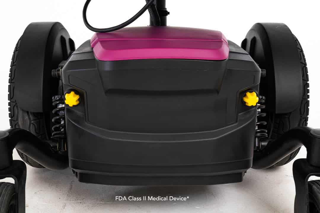 Close-up of a black and pink Jazzy® EVO 614HD Power Chair featuring thick rubber wheels and yellow knobs on each side. Text at the bottom reads, FDA Class II Medical Device.