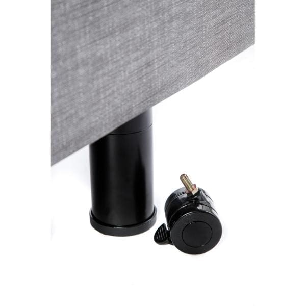 Close-up of a black cylindrical furniture leg attached to the Passport Hi Low Adjustable Beds gray upholstered base, with a detached black caster wheel lying on the floor next to it.