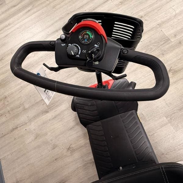 A view from above the handlebars of a Pride Go Go Elite Traveller Gen 3 4-Wheel Scooter, showing the control console with a speed dial, battery gauge, and a front-mounted storage basket.