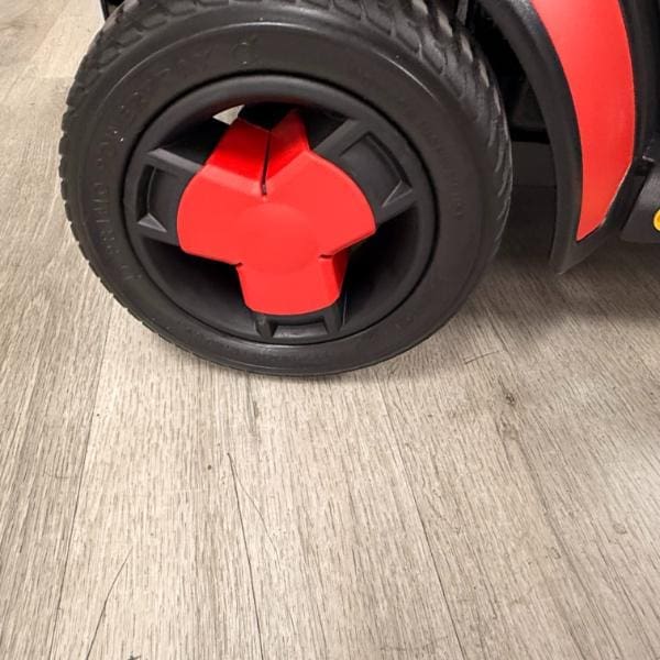 Black wheel with a red three-spoke hubcap on a Pride Go Go Elite Traveller Gen 3 4-Wheel Scooter.